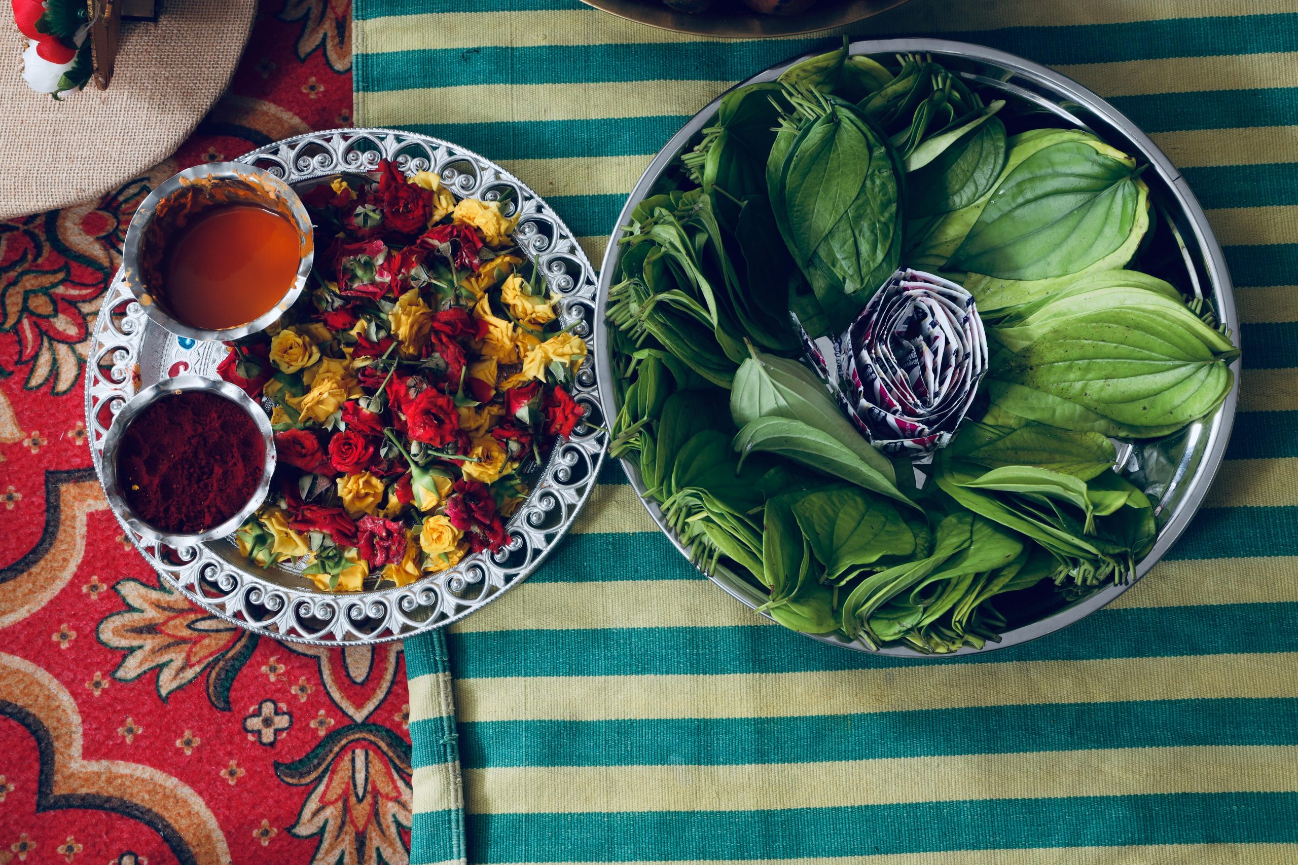 Vibrant display of fresh leaves and flower petals used in traditional ceremonies on a striped background.